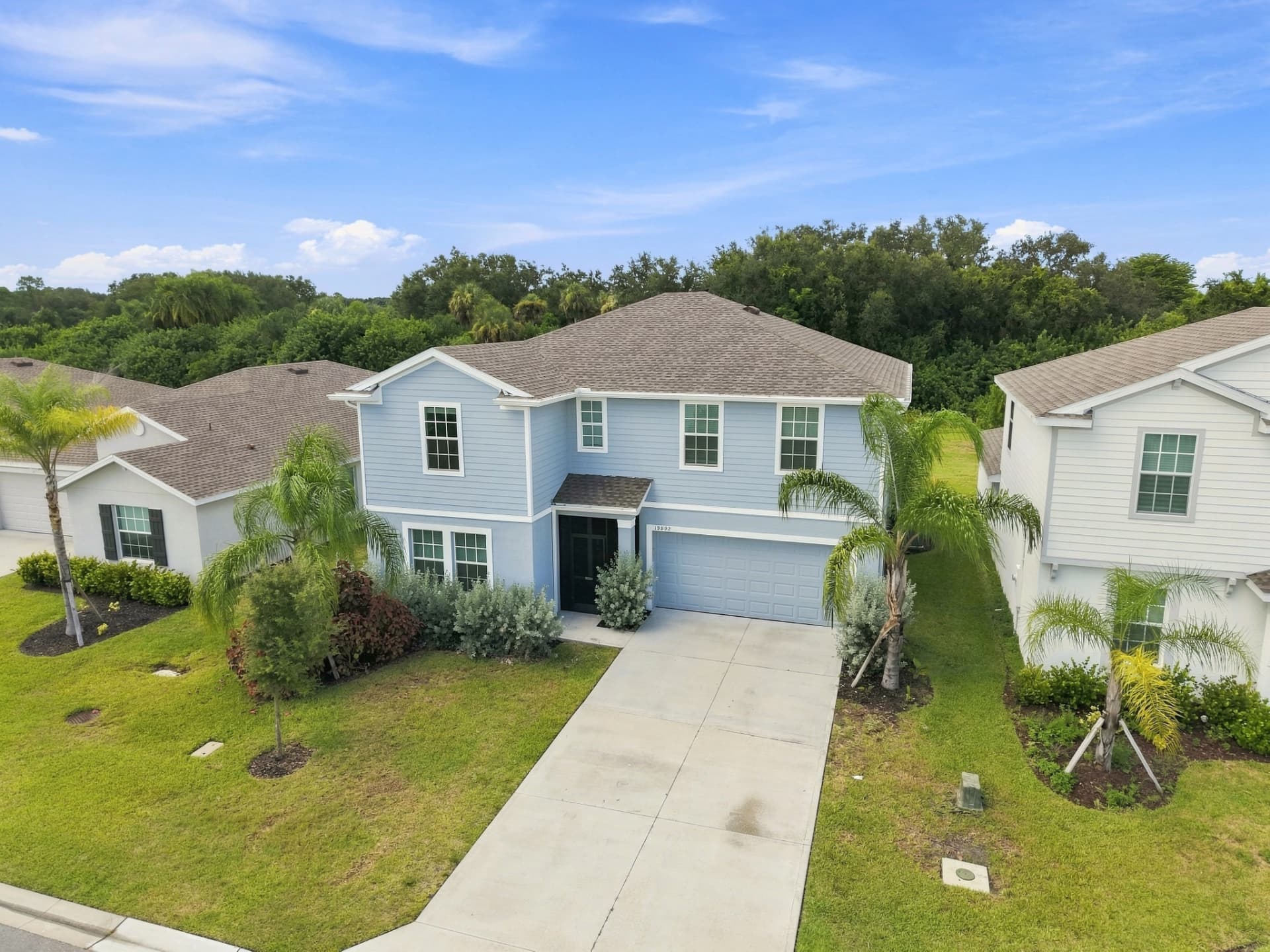 Drone photo of a light blue two-story Florida home with palm trees and concrete driveway
